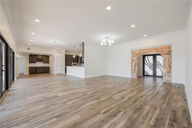 unfurnished living room with an inviting chandelier, crown molding, light wood-type flooring, and french doors