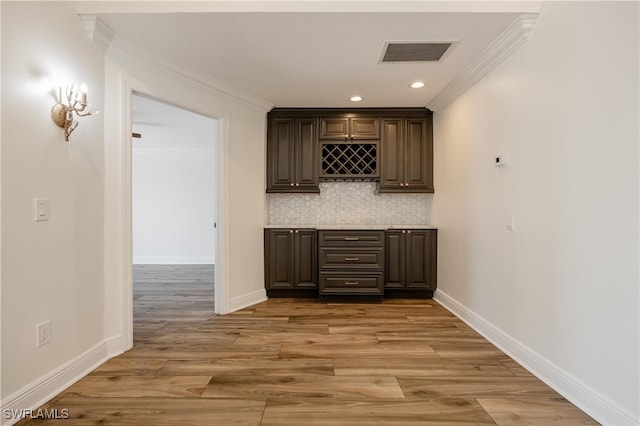 bar with light hardwood / wood-style floors, tasteful backsplash, dark brown cabinetry, and crown molding