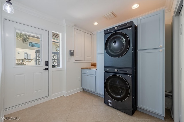 laundry room featuring cabinets, light tile patterned flooring, ornamental molding, and stacked washer / dryer