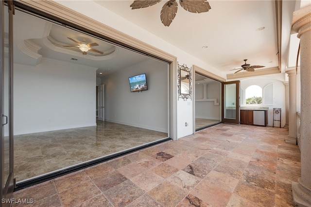 hallway featuring a raised ceiling, decorative columns, and ornamental molding