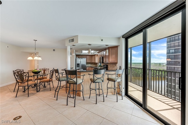 kitchen with light tile patterned floors, stainless steel refrigerator with ice dispenser, decorative light fixtures, expansive windows, and kitchen peninsula