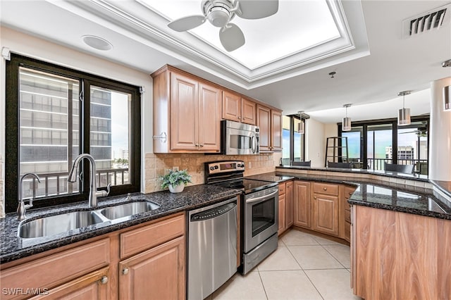 kitchen with a raised ceiling, sink, decorative light fixtures, appliances with stainless steel finishes, and dark stone counters