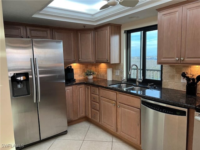 kitchen with sink, dark stone counters, appliances with stainless steel finishes, and a tray ceiling