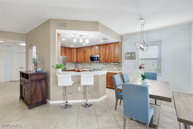 kitchen featuring a breakfast bar area, decorative light fixtures, light tile patterned floors, appliances with stainless steel finishes, and tasteful backsplash