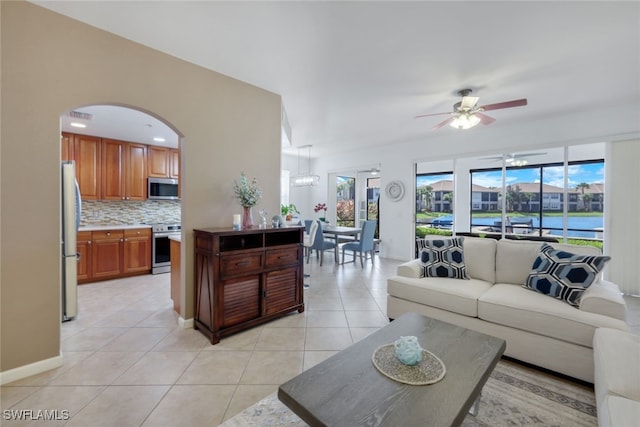 living room with a water view, ceiling fan with notable chandelier, and light tile patterned floors