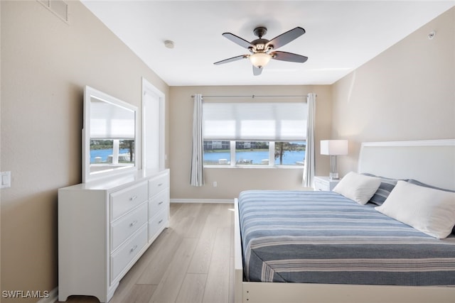 bedroom with multiple windows, ceiling fan, a water view, and light wood-type flooring