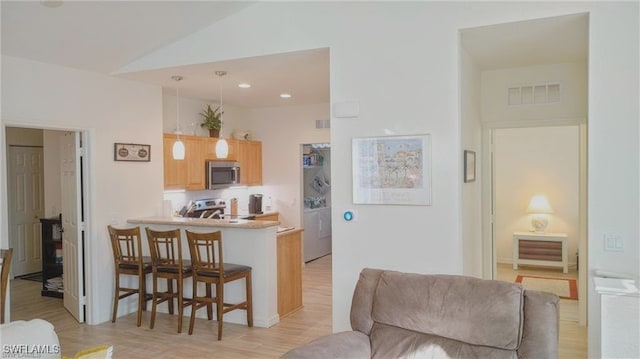 kitchen featuring lofted ceiling, a breakfast bar area, kitchen peninsula, light brown cabinetry, and light hardwood / wood-style floors