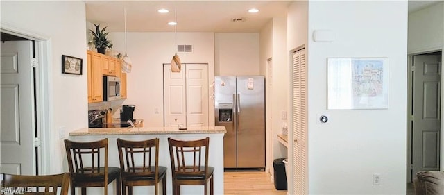 kitchen with light hardwood / wood-style flooring, kitchen peninsula, a breakfast bar, light brown cabinetry, and appliances with stainless steel finishes