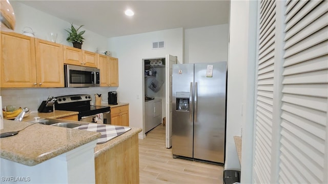 kitchen with light brown cabinetry, kitchen peninsula, light hardwood / wood-style floors, stainless steel appliances, and light stone counters