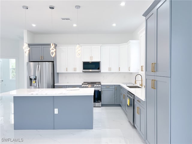 kitchen with appliances with stainless steel finishes, sink, a center island, hanging light fixtures, and white cabinetry