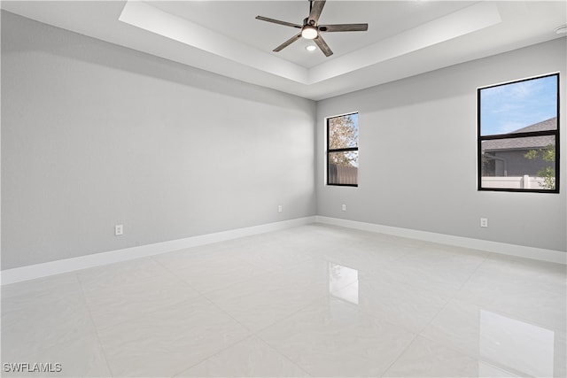 spare room with a healthy amount of sunlight, a tray ceiling, and ceiling fan