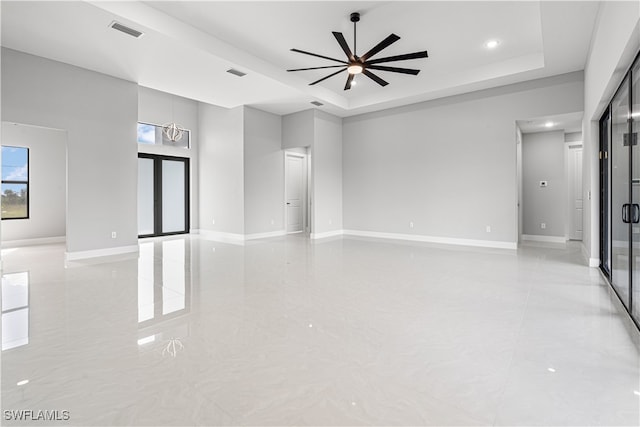 empty room with light tile patterned flooring, ceiling fan, and a raised ceiling