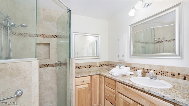 bathroom featuring a shower with shower door, vanity, and backsplash