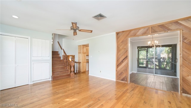 living room featuring ornamental molding, hardwood / wood-style floors, ceiling fan with notable chandelier, and wooden walls