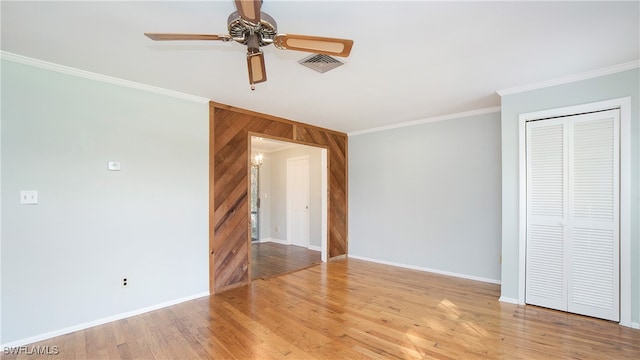 interior space featuring wooden walls, ornamental molding, ceiling fan, a closet, and light wood-type flooring