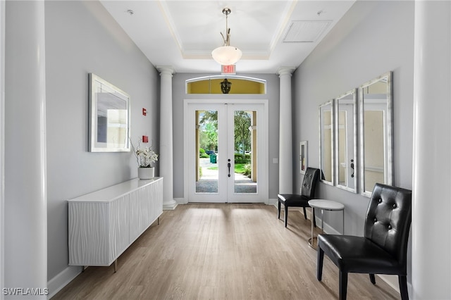 doorway featuring a tray ceiling, french doors, ornate columns, and light hardwood / wood-style flooring