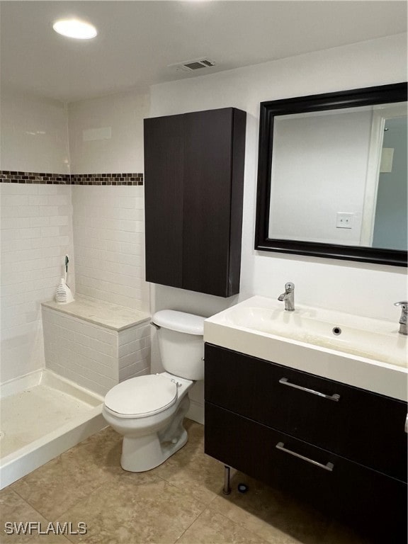 bathroom with tile patterned floors, vanity, toilet, and a tile shower