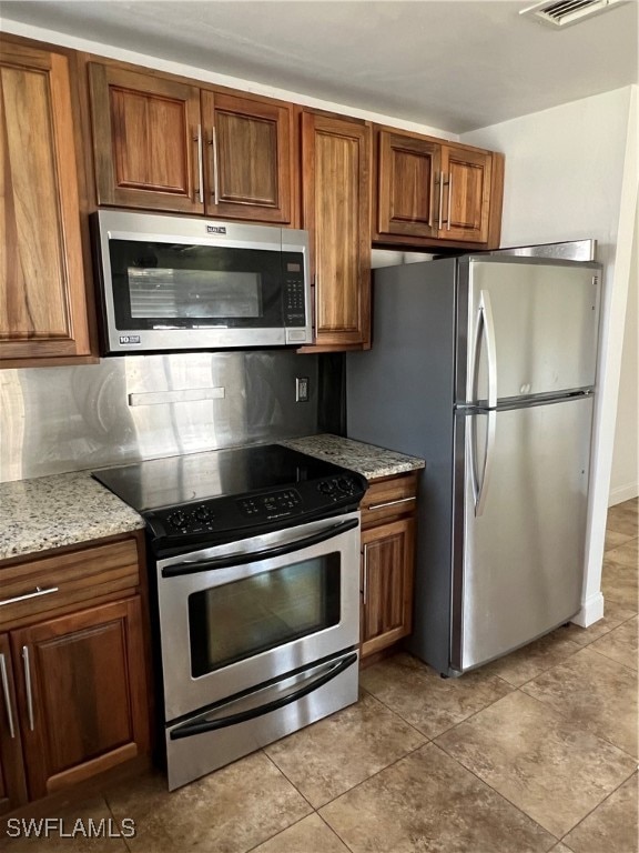 kitchen featuring appliances with stainless steel finishes, light tile patterned flooring, tasteful backsplash, and light stone countertops