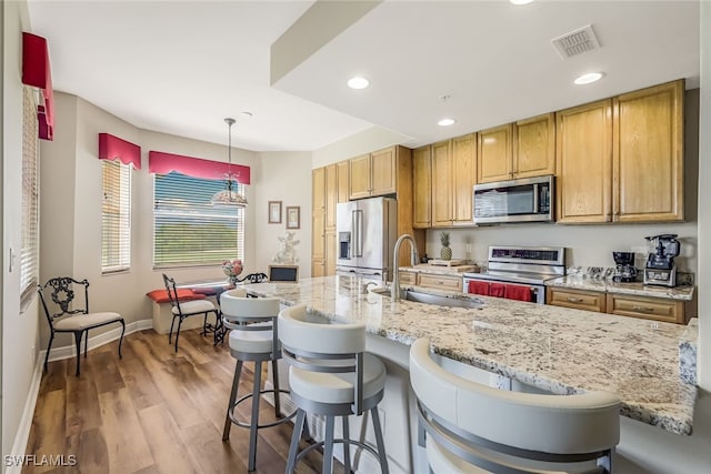 kitchen featuring a breakfast bar, stainless steel appliances, sink, light hardwood / wood-style floors, and decorative light fixtures