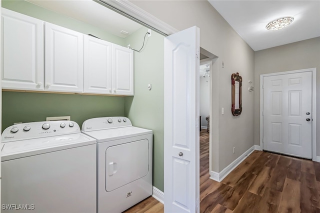 washroom with dark wood-type flooring, washing machine and dryer, and cabinets