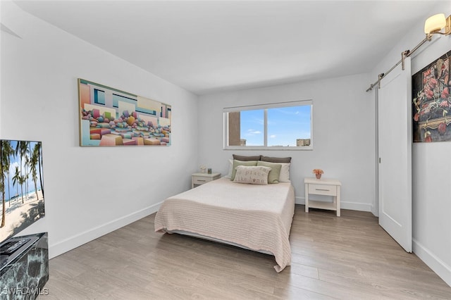 bedroom with a barn door and light hardwood / wood-style floors