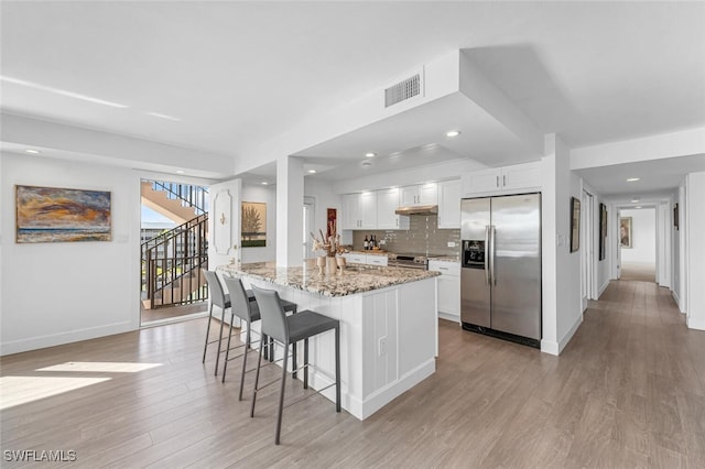 kitchen featuring a kitchen island with sink, white cabinets, light stone countertops, appliances with stainless steel finishes, and light hardwood / wood-style floors