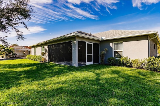 back of property featuring a sunroom, a lawn, and stucco siding