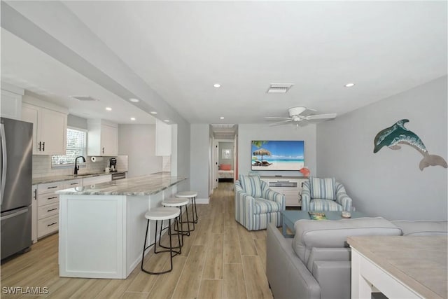 kitchen featuring light stone countertops, a breakfast bar, light hardwood / wood-style flooring, white cabinets, and stainless steel refrigerator