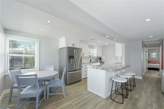 kitchen featuring stainless steel fridge, white cabinetry, sink, and light hardwood / wood-style flooring