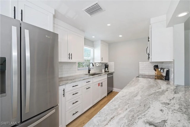 kitchen with sink, stainless steel appliances, tasteful backsplash, white cabinets, and light wood-type flooring