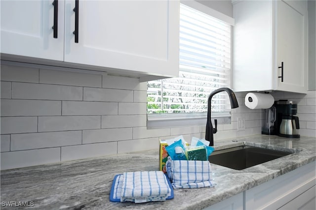 kitchen featuring decorative backsplash, light stone countertops, white cabinetry, and sink