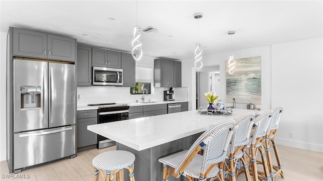 kitchen with gray cabinets, stainless steel appliances, tasteful backsplash, pendant lighting, and sink