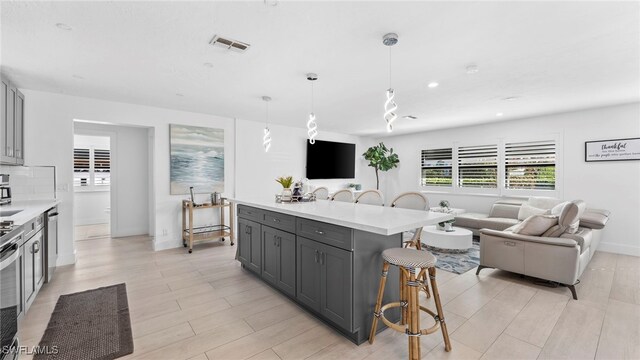 kitchen with pendant lighting, a center island, stainless steel dishwasher, gray cabinetry, and a breakfast bar area