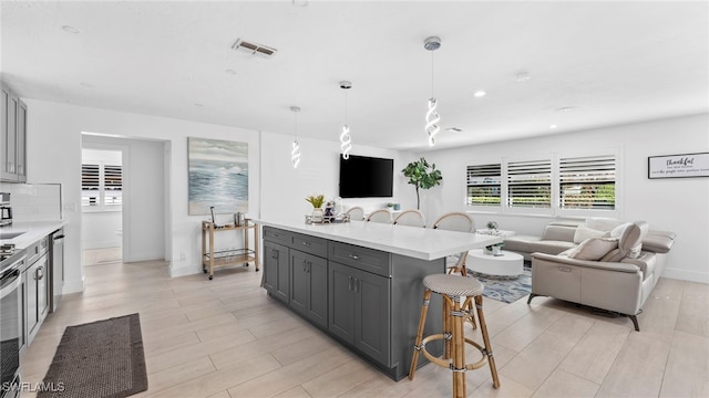 kitchen with a breakfast bar area, gray cabinetry, a center island, dishwasher, and pendant lighting