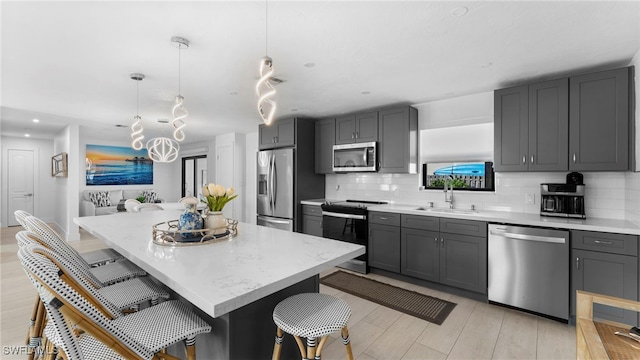 kitchen with sink, a breakfast bar area, hanging light fixtures, appliances with stainless steel finishes, and a kitchen island