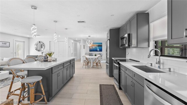 kitchen with decorative light fixtures, decorative backsplash, sink, gray cabinetry, and stainless steel appliances