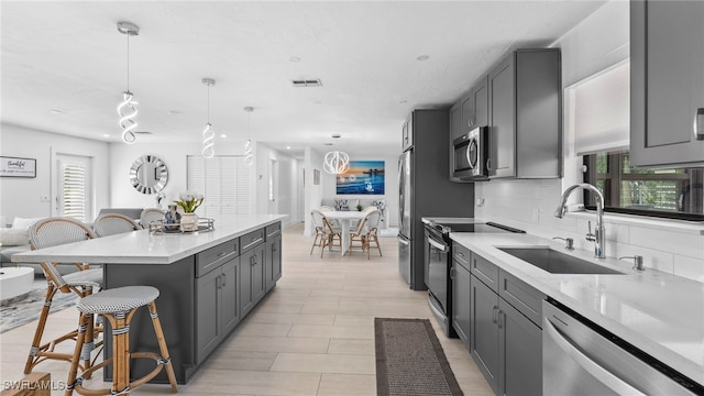 kitchen with appliances with stainless steel finishes, decorative light fixtures, sink, gray cabinetry, and a center island