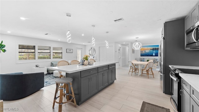 kitchen featuring electric range oven, a center island, hanging light fixtures, gray cabinetry, and a breakfast bar area