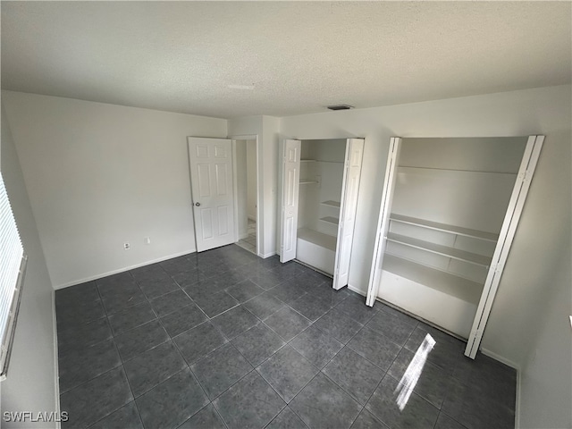 unfurnished bedroom with dark tile patterned flooring and a textured ceiling