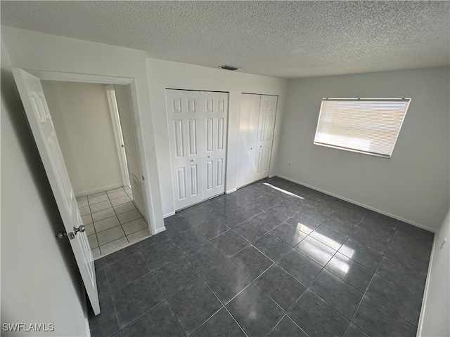 unfurnished bedroom with dark tile patterned flooring, multiple closets, and a textured ceiling