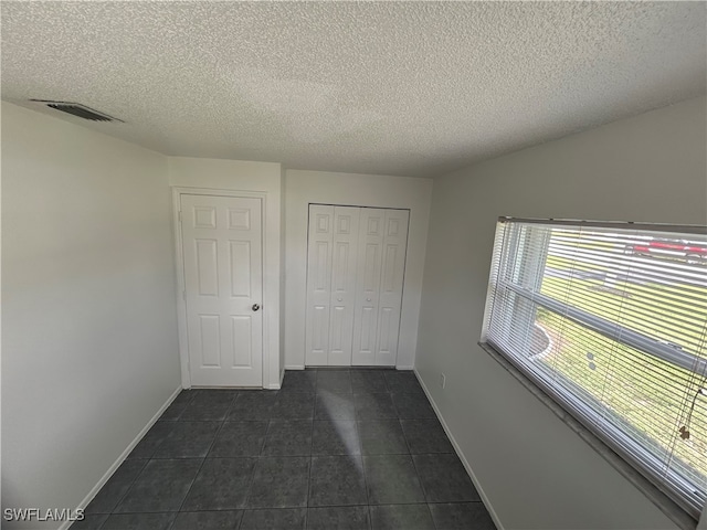 unfurnished bedroom with a textured ceiling, a closet, and dark tile patterned flooring