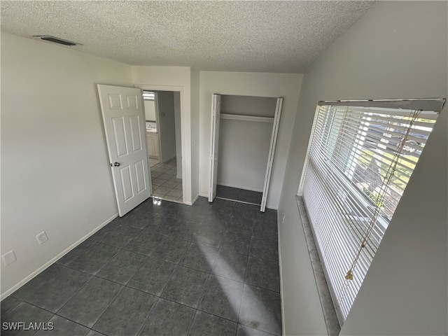 unfurnished bedroom featuring a closet, a textured ceiling, and dark tile patterned flooring