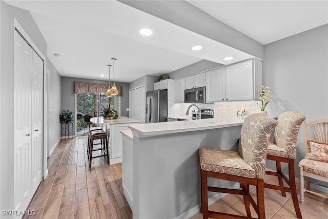 kitchen featuring hanging light fixtures, kitchen peninsula, a breakfast bar, appliances with stainless steel finishes, and light hardwood / wood-style floors