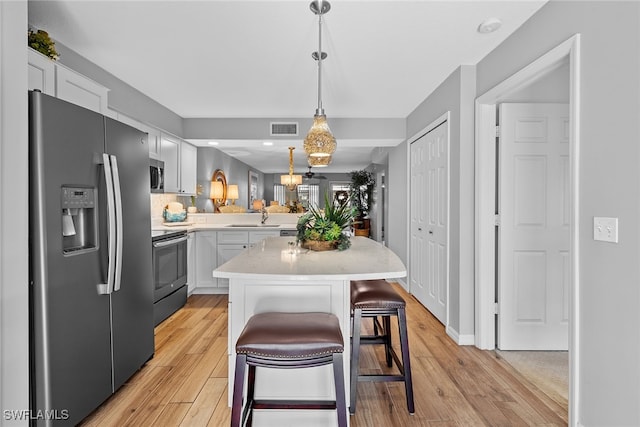 kitchen with a breakfast bar area, kitchen peninsula, stainless steel appliances, light wood-type flooring, and white cabinetry