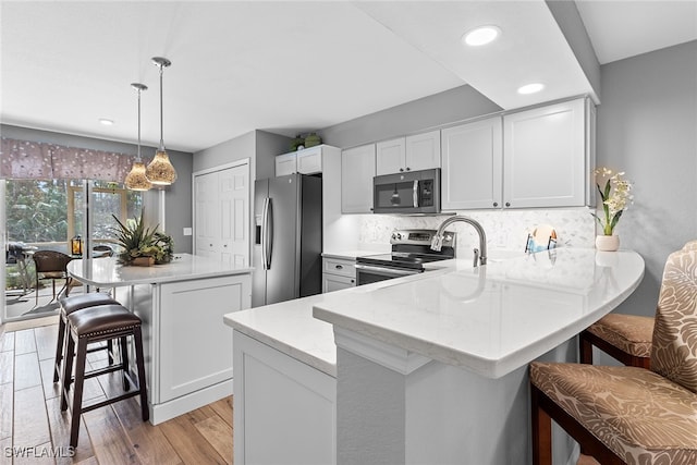 kitchen featuring kitchen peninsula, a kitchen breakfast bar, light wood-type flooring, pendant lighting, and stainless steel appliances