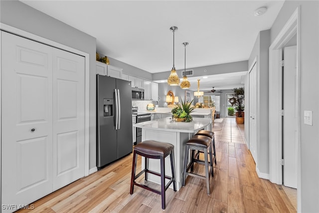 kitchen with appliances with stainless steel finishes, a kitchen bar, white cabinetry, light hardwood / wood-style floors, and decorative backsplash