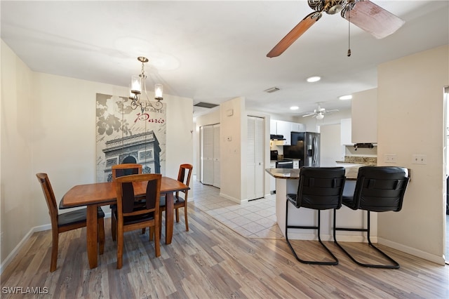 dining room with ceiling fan with notable chandelier and light hardwood / wood-style floors