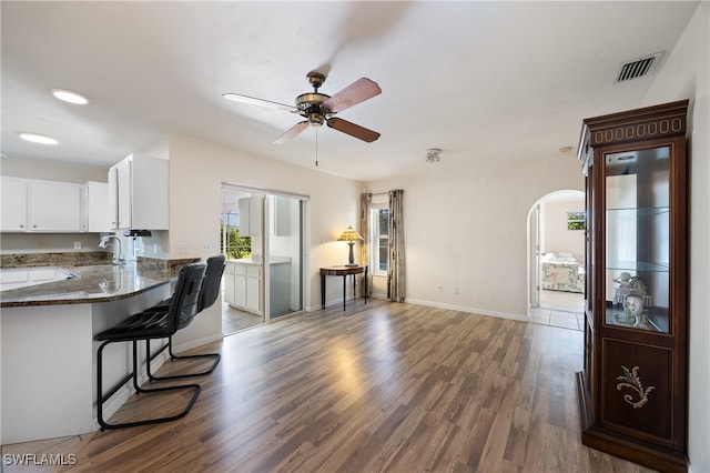 kitchen with kitchen peninsula, white cabinets, ceiling fan, dark hardwood / wood-style flooring, and a kitchen bar