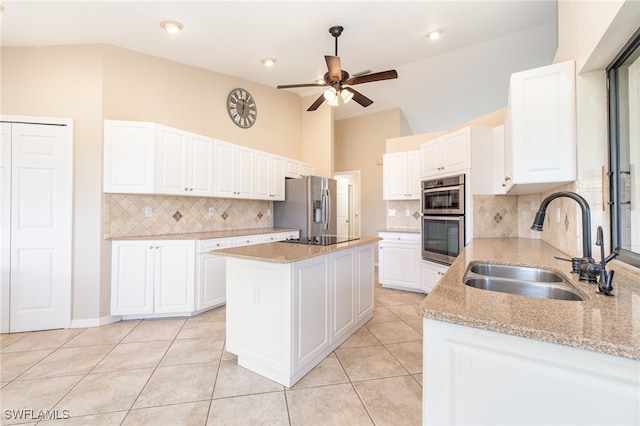 kitchen with light stone counters, a kitchen island, appliances with stainless steel finishes, white cabinetry, and sink