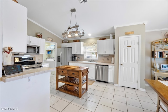 kitchen featuring washer and clothes dryer, sink, white cabinets, pendant lighting, and appliances with stainless steel finishes